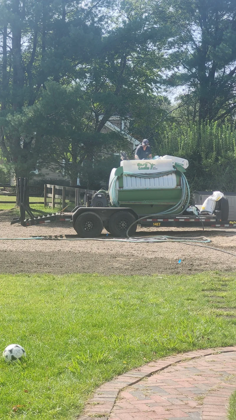 A crew member working beside hydroseeding equipment at a lawn project.
