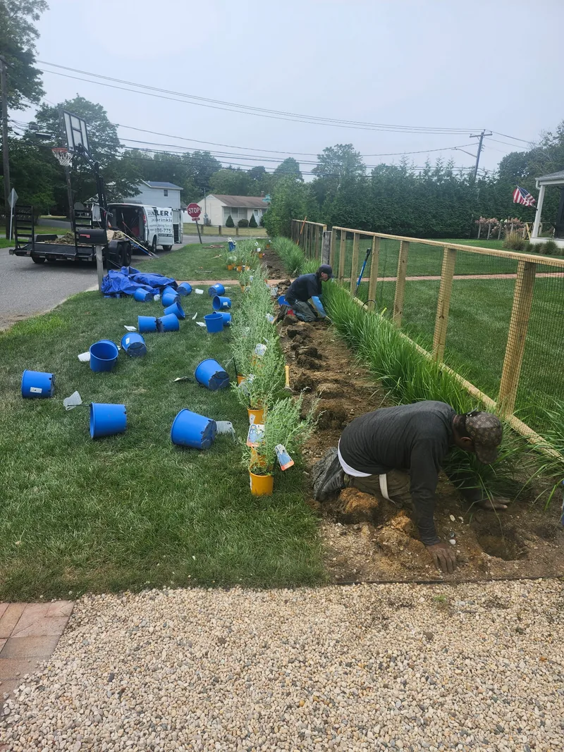 Installation work along a new planting bed beside a split-rail fence.